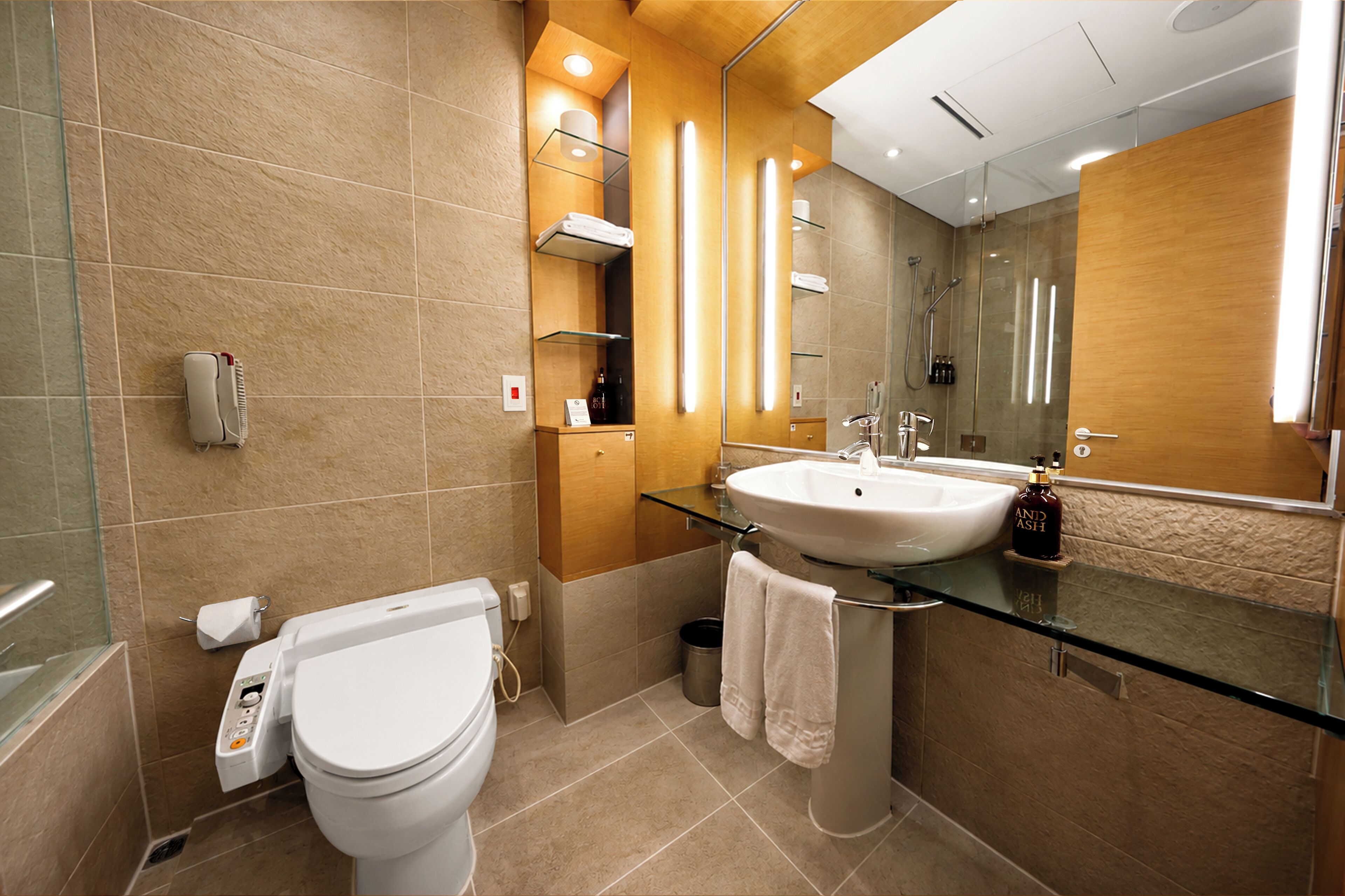 A modern bathroom with a glass sink, a white toilet, and a large mirror.