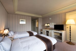 Quarto de hotel com duas camas, uma escrivaninha com televisão, um abajur e um guarda-roupa.