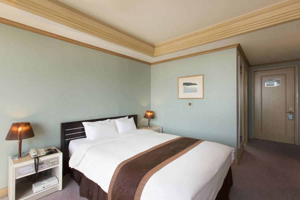 A hotel room with a bed, bedside lamps, a nightstand, a framed picture on the wall, and a door.
