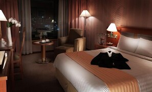 A hotel room with a large bed, a chair, a small table, and a lamp.