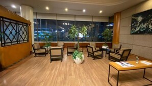 A modern hotel lobby with wooden flooring, comfortable seating, large windows offering city views, and a central plant. - Hotel Paragon (Busan)