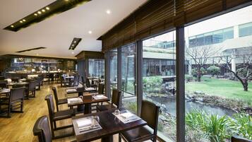 Um restaurante moderno com mesas e cadeiras de madeira, grandes janelas com vista para um jardim.