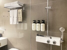 A modern bathroom with a shower, a towel rack with folded towels, and three toiletries (body wash, conditioner, shampoo) mounted on the wall.