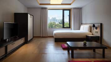 A modern hotel room with a large bed, a TV, a desk, and a view of the city.