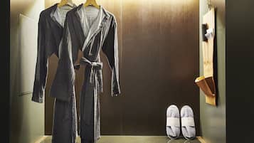 Quarto de hotel com armário de madeira, chinelos e duas roupões pendurados em um suporte.