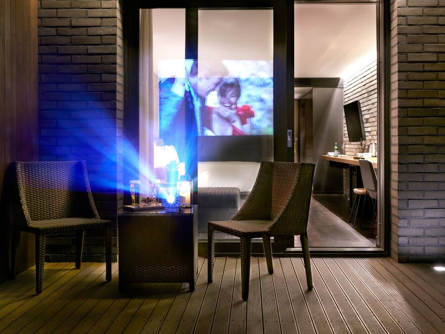 A cozy outdoor seating area with wicker chairs and a small table, featuring a television screen displaying a scene.