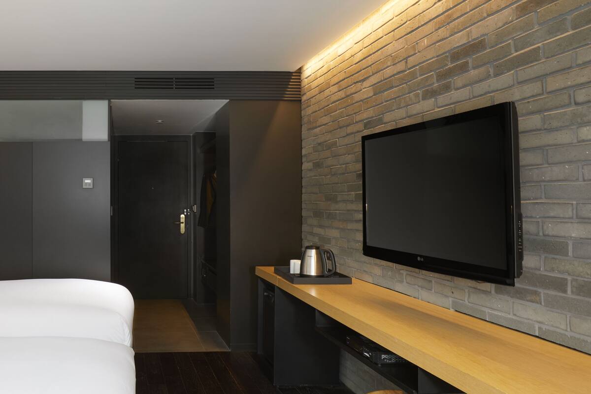 Een moderne hotelkamer met een groot bed, een flatscreen televisie aan een bakstenen muur en een houten console tafel.