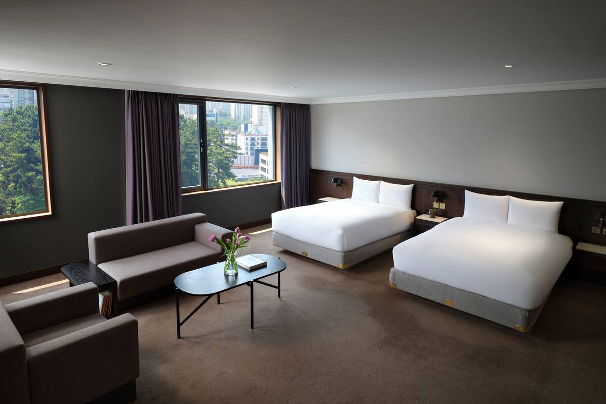 Een hotelkamer met twee bedden, een bank, een bijzettafeltje en uitzicht op de stad.