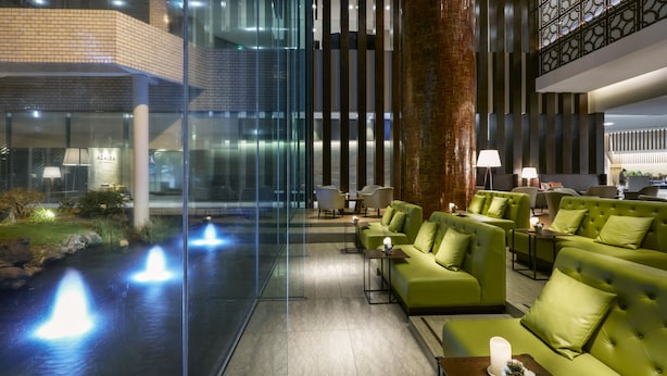 Un vestíbulo moderno con asientos verdes, un muro de cristal y una fuente de agua.