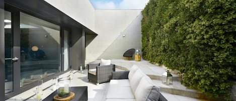 A modern outdoor seating area with wicker furniture, a white sofa, and a glass door leading to a patio.