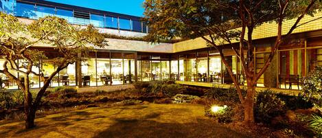 A modern building with a glass facade, outdoor seating area, and a well-maintained garden.