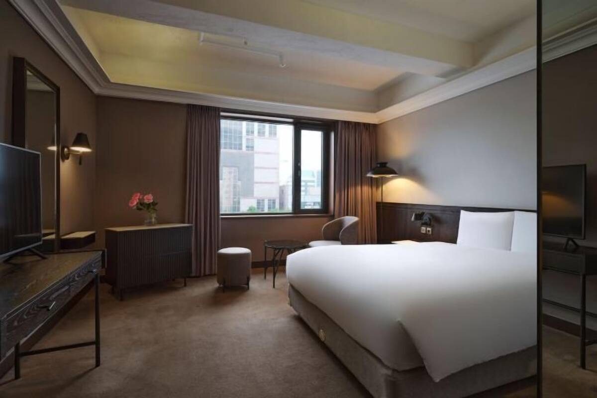 Een hotelkamer met een groot bed, een bureau, een stoel, een klein tafeltje, een televisie en een raam met gordijnen.