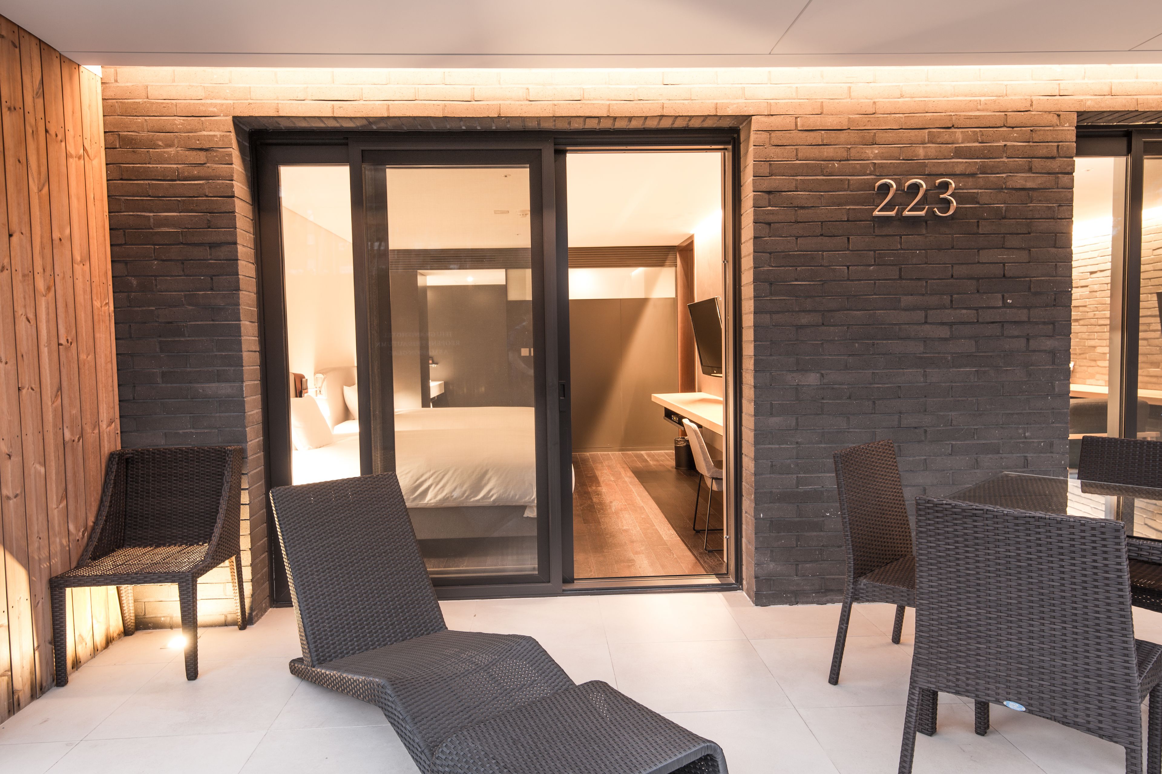 A modern hotel room with a sliding glass door leading to a bathroom, a bed, and a desk with a chair.