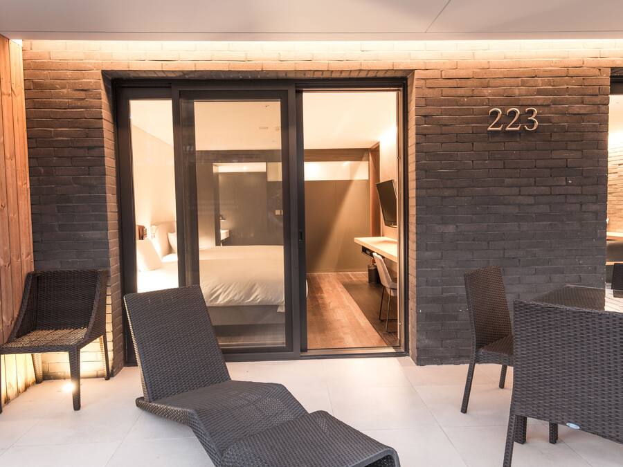 A modern hotel room with a sliding glass door leading to a bathroom, a bed, and a desk with a chair.