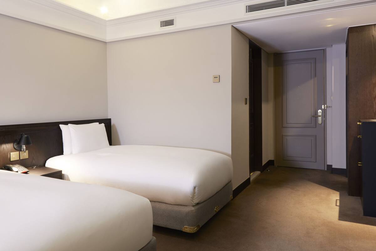 Een hotelkamer met twee bedden, een bureau en een flatscreen televisie, en een deur naar een andere kamer.
