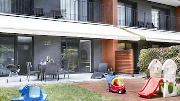 A modern building with a balcony, outdoor seating, and children's play equipment.