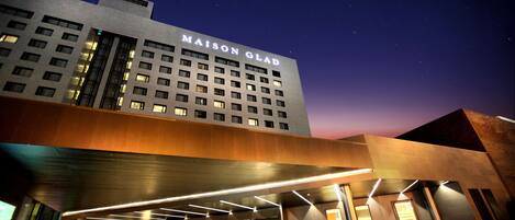 A modern hotel with a prominent sign reading "MAISON GLAD" and a covered entrance area.