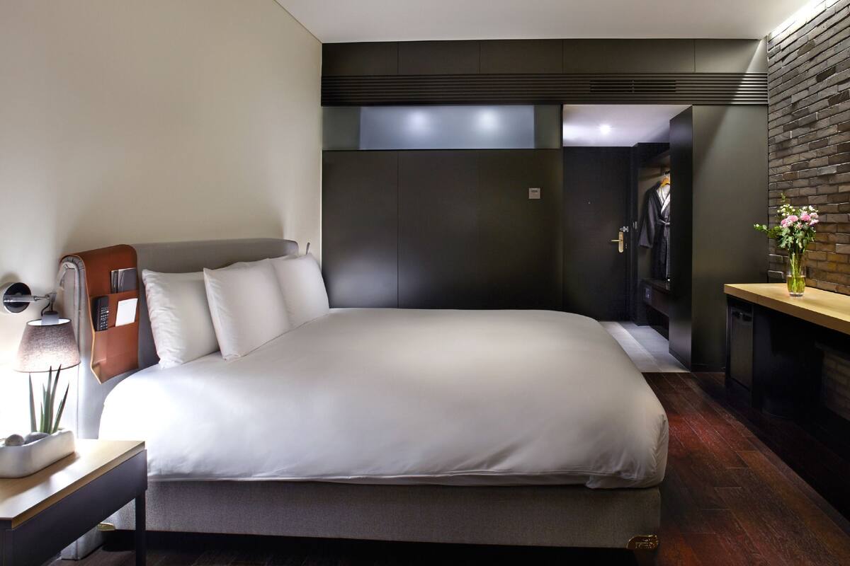 Een moderne hotelkamer met een groot bed, een bureau met een lamp, een televisie en een bakstenen muur.