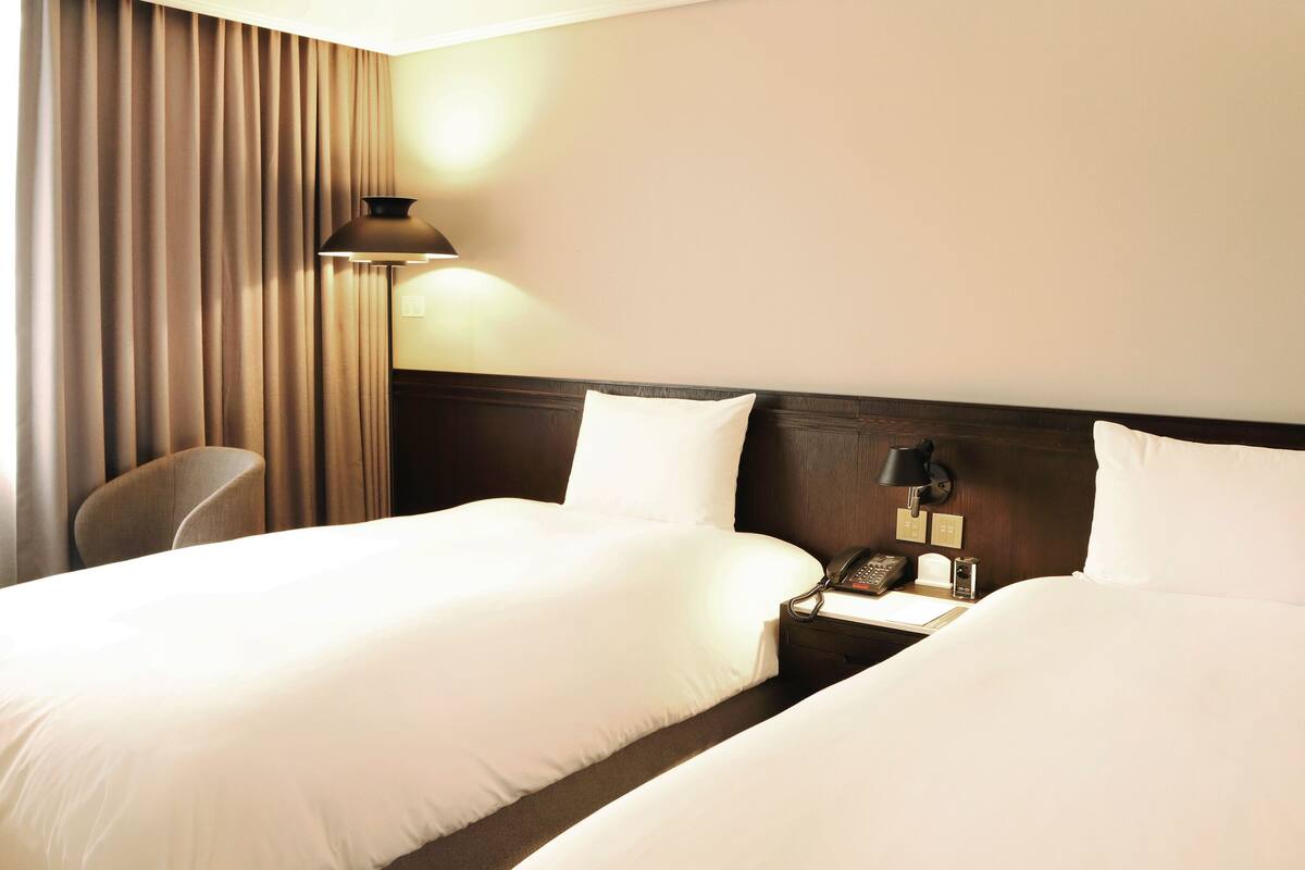 Een hotelkamer met twee bedden, een bureau met telefoon, een lamp en een stoel.