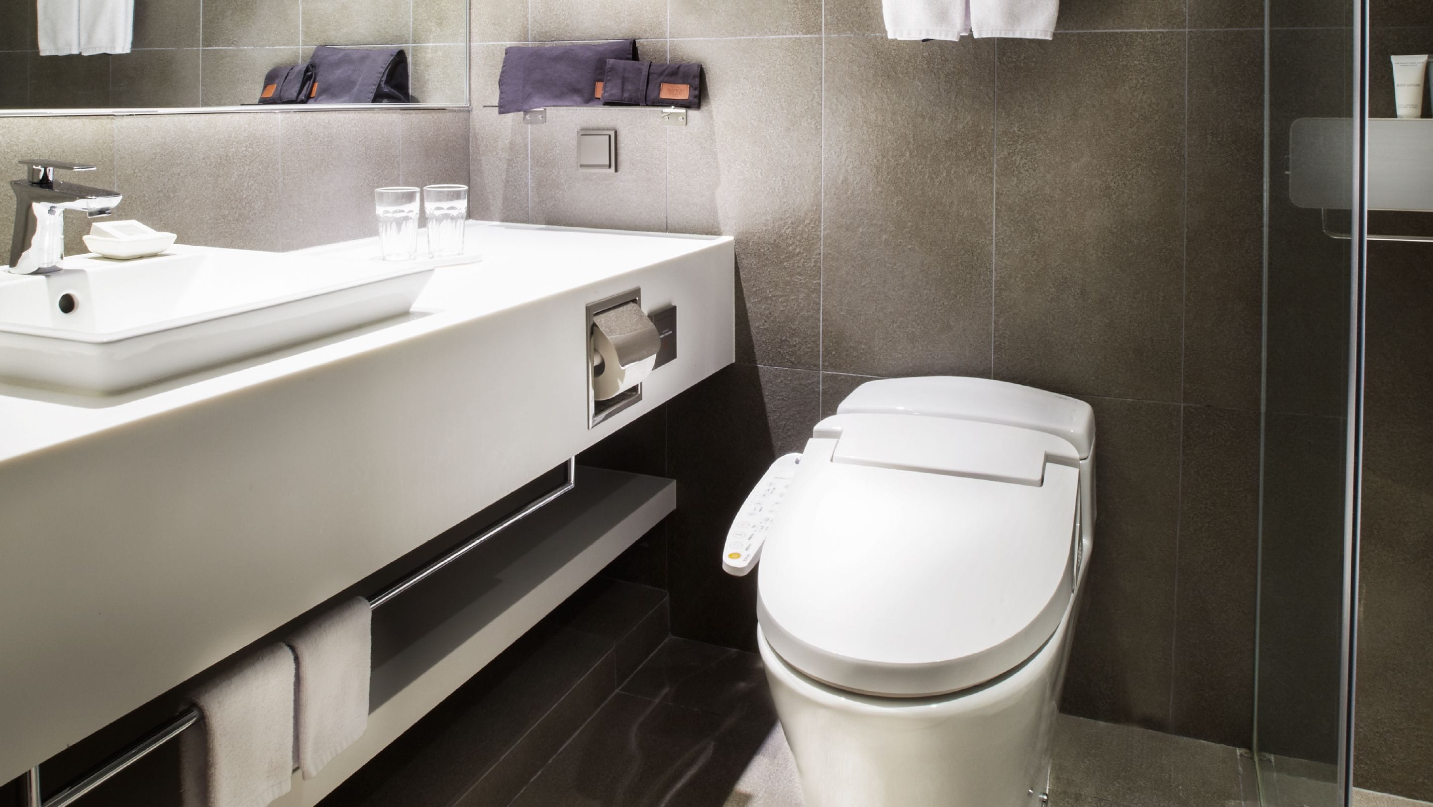 A modern bathroom with a white sink, mirror, and toilet. There are towels and a soap dispenser on the sink.