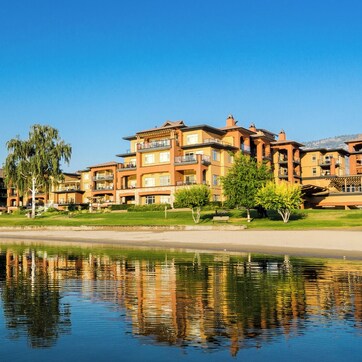 A multi-story hotel with balconies, a reflective water body in front, and a clear sky.