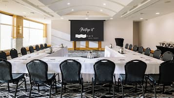 A conference room with a long table, multiple chairs, and a presentation screen in a hotel setting.