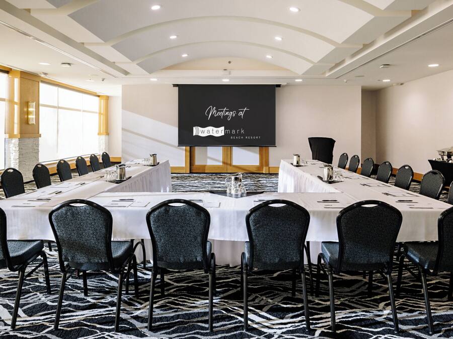A conference room with a long table, multiple chairs, and a presentation screen in a hotel setting.