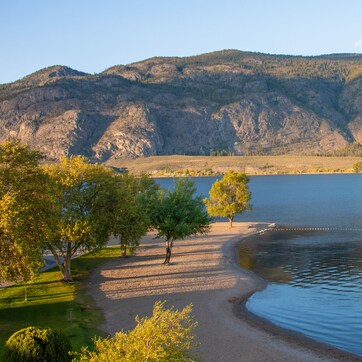 A lakeside view with a mountain backdrop, a clear sky, and a small dock extending into the water.