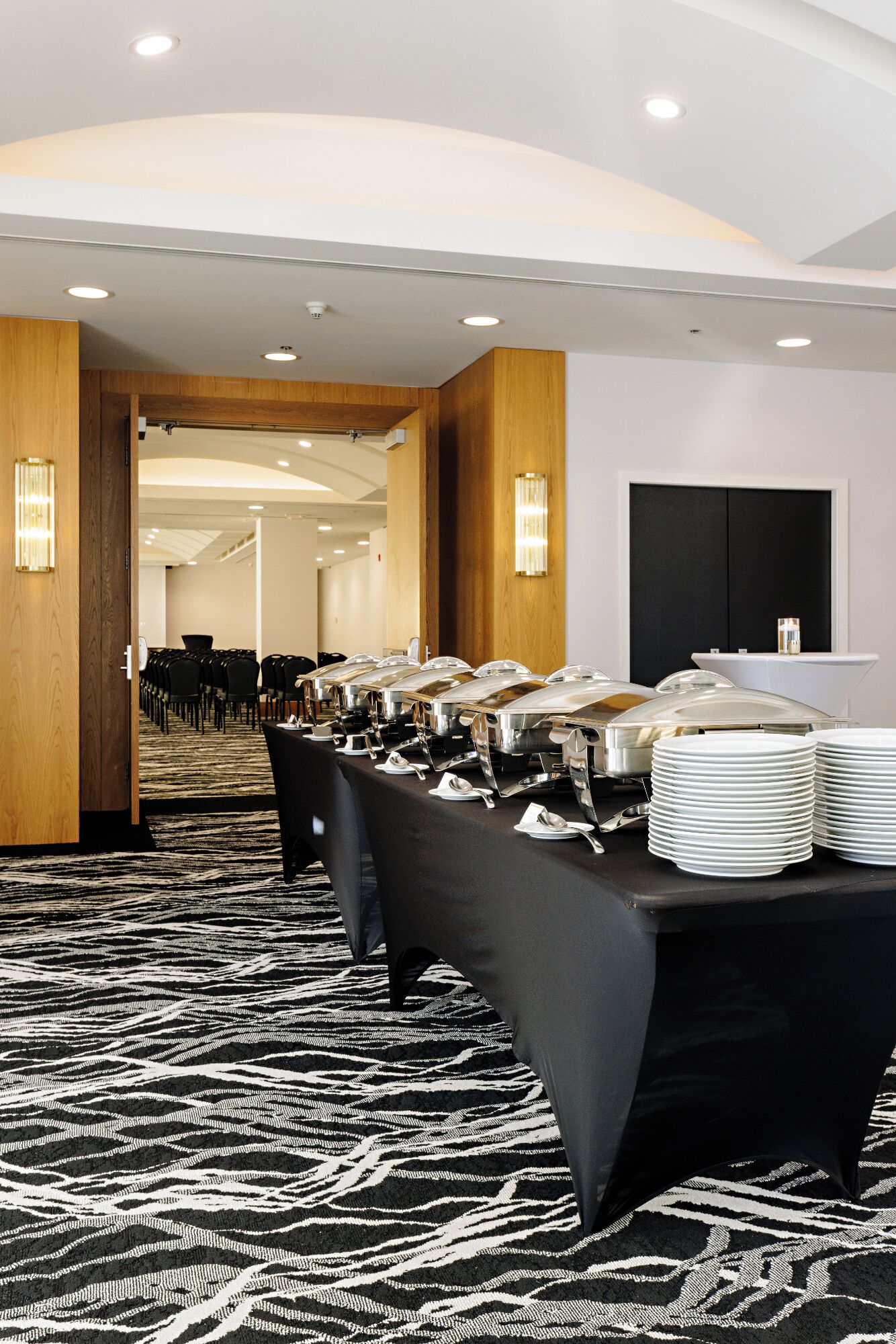 A conference room with a long table set for a buffet, chairs lined up, and a carpeted floor.
