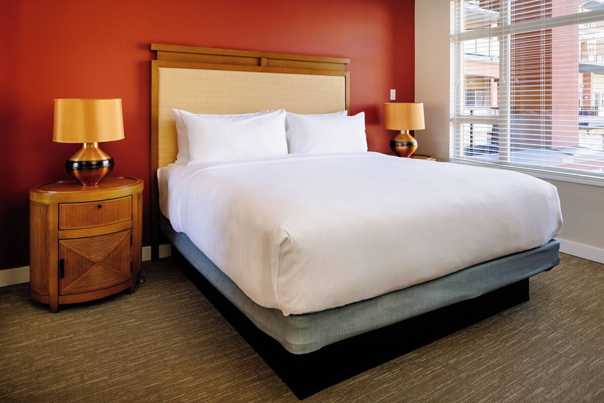 A hotel room with a large bed, two bedside tables with lamps, and a window with blinds.