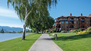 A pathway leading to a building with balconies, a lake, and greenery.