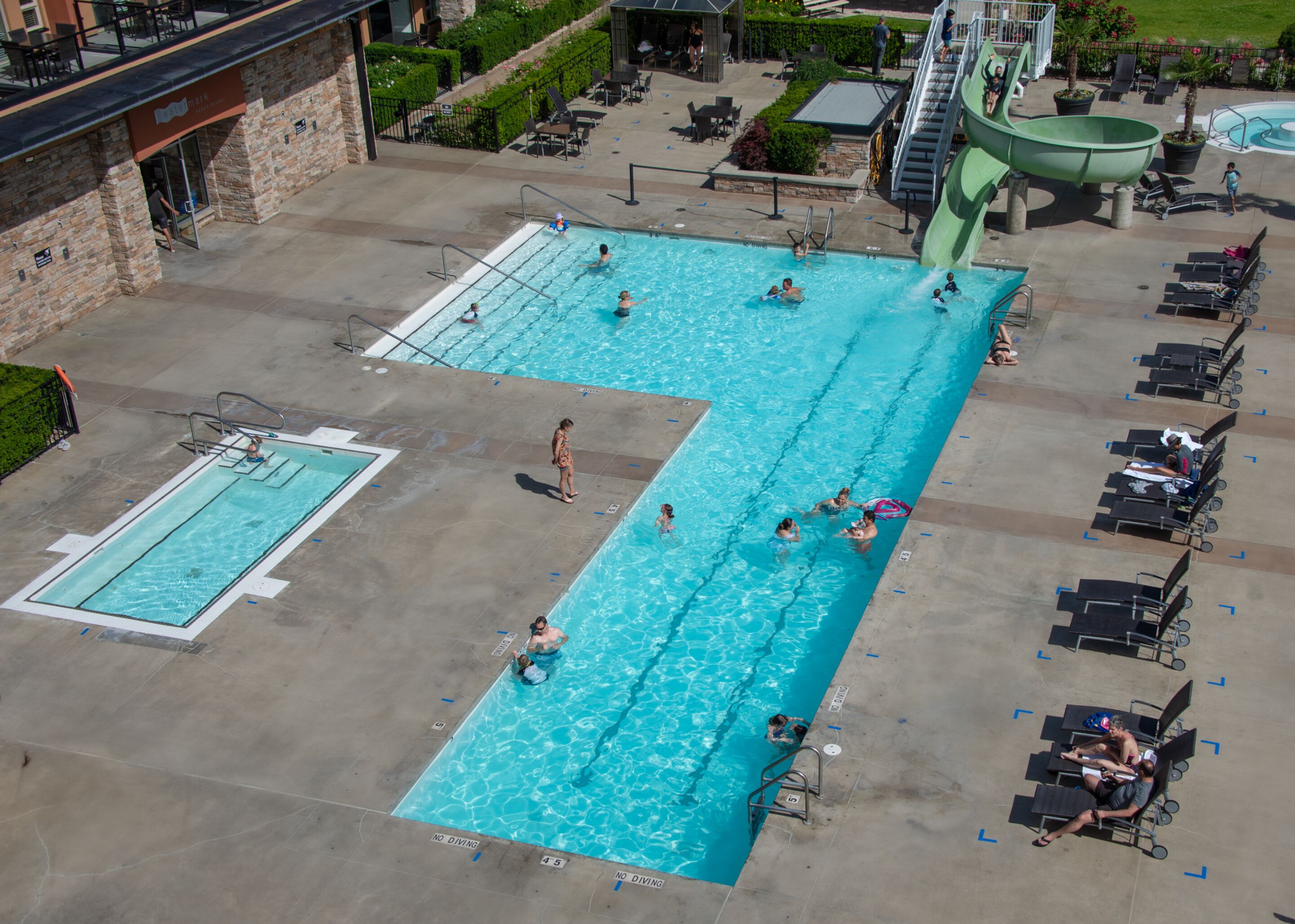 Una gran piscina al aire libre con múltiples carriles, una piscina más pequeña separada y un tobogán de agua.