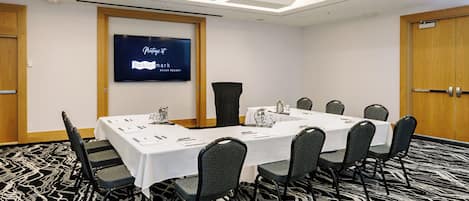 A conference room with a long table, chairs, a projector screen, and a carpeted floor.