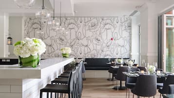 A modern restaurant with a long counter, black chairs, and a floral wall mural.
