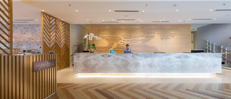 A reception desk with a marble top, a receptionist, and a herringbone patterned floor.