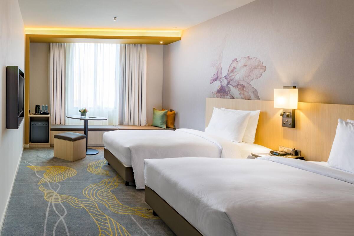 A hotel room with two beds, a small desk, a seating area, and a painting on the wall.
