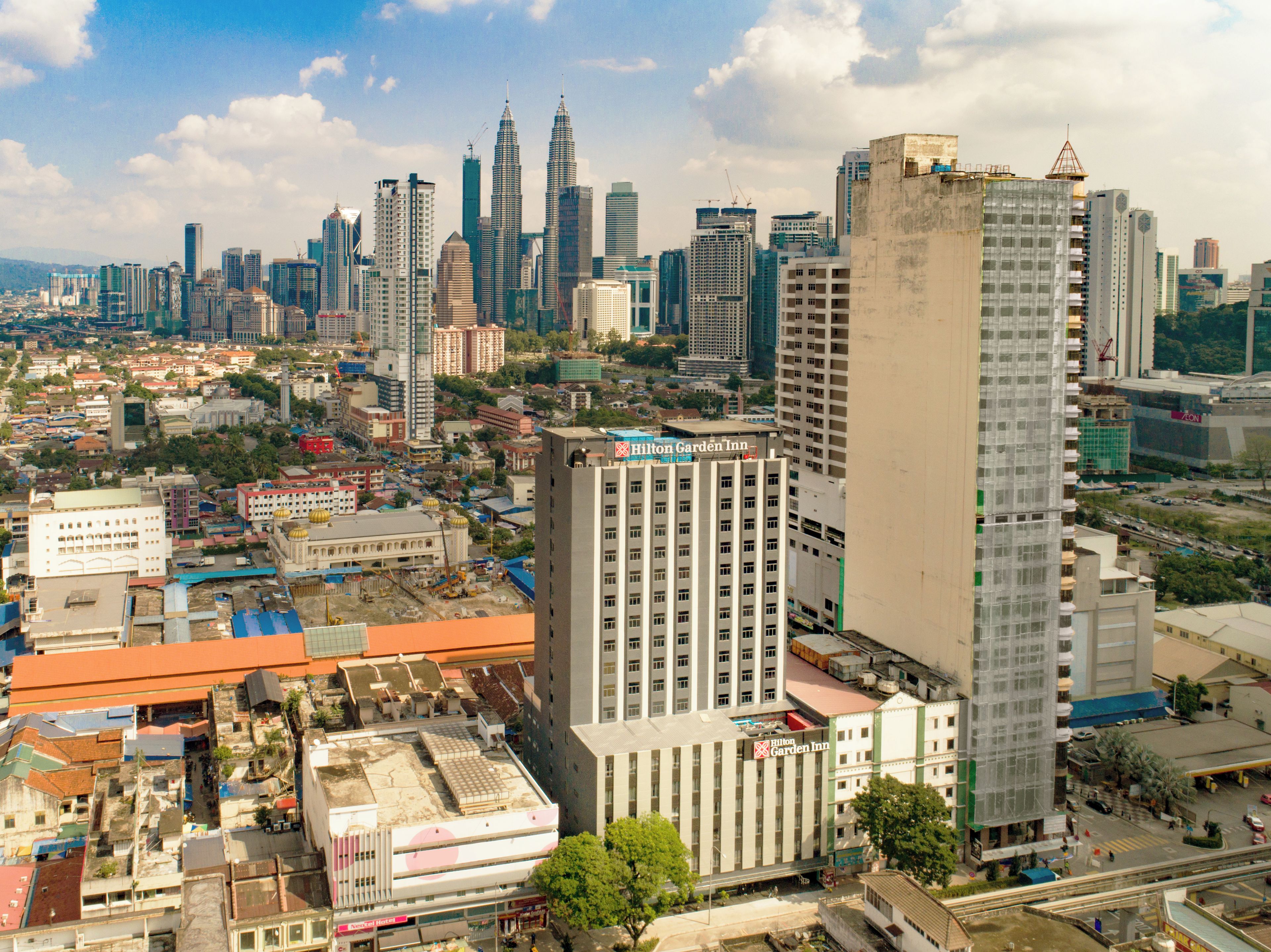 A cityscape with a prominent Hilton Garden Inn hotel, surrounded by high-rise buildings and a busy street.