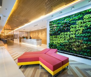 A modern lobby with a reception desk, a large green wall with plants, and a red and yellow sectional sofa. - Hilton Garden Inn Kuala Lumpur Jalan Tuanku Abdul Rahman North (Kuala Lumpur)