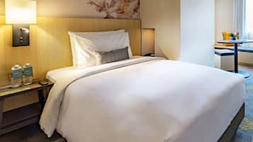 A hotel room with a large bed, a nightstand with a lamp, a wall-mounted phone, and a small table with a vase.