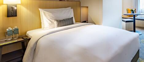 A hotel room with a large bed, a nightstand with a lamp, a wall-mounted phone, and a small table with a vase.