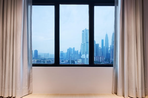 A window with a view of a cityscape, curtains, and a plain wall.