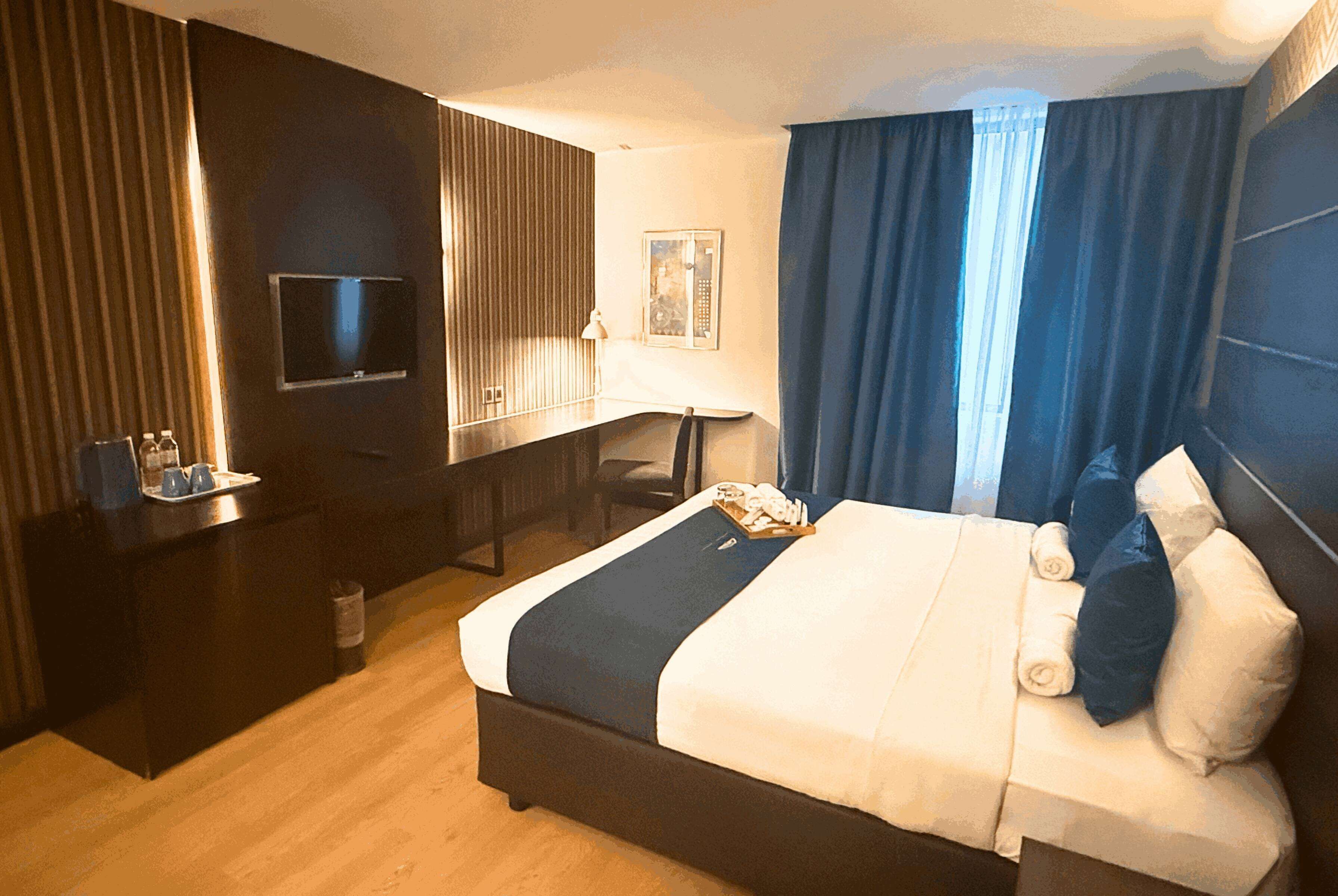 Una habitación de hotel con cama, escritorio, televisión y un minibar.