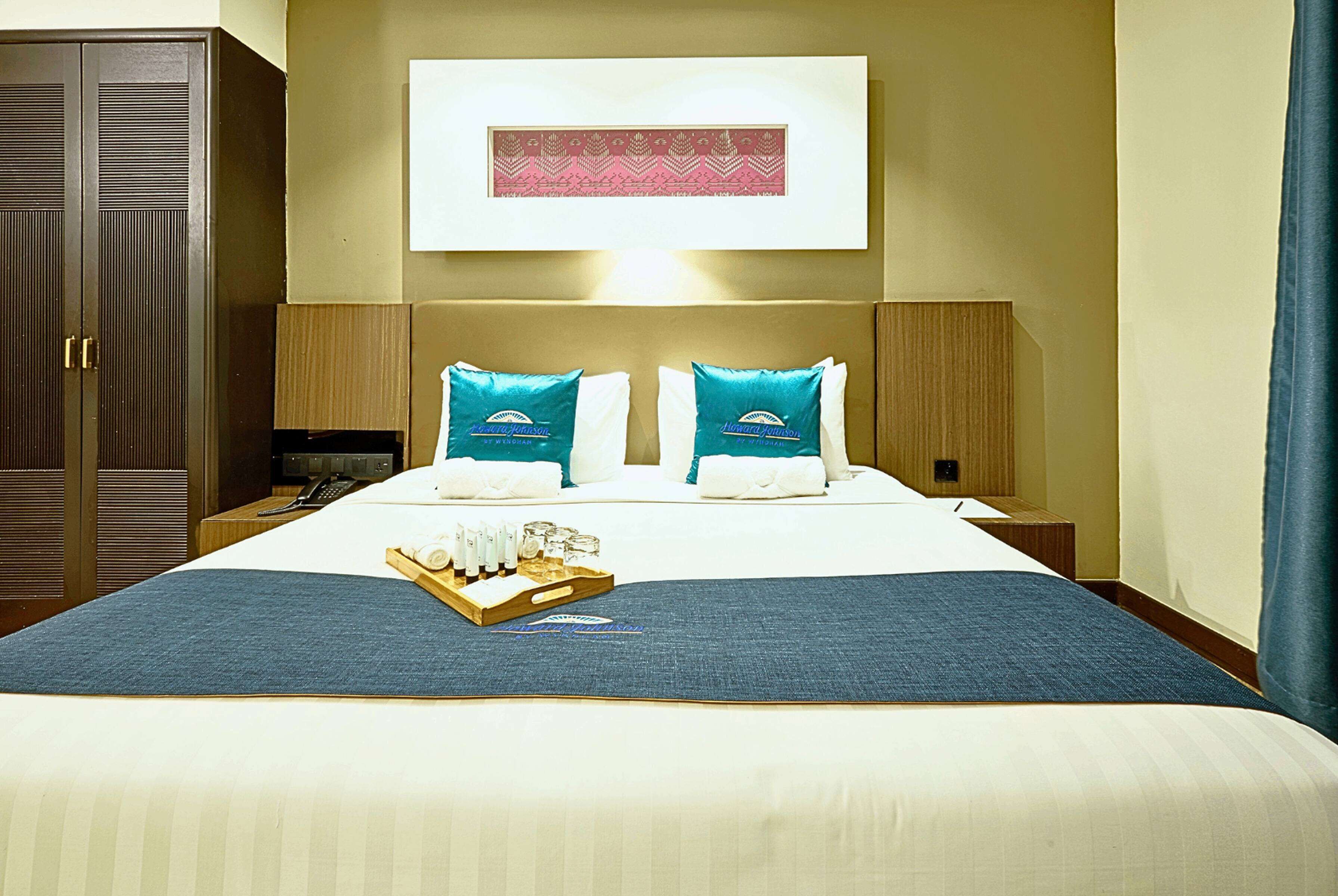 A hotel room with a large bed, two pillows, a tray with toiletries, and a framed picture on the wall.