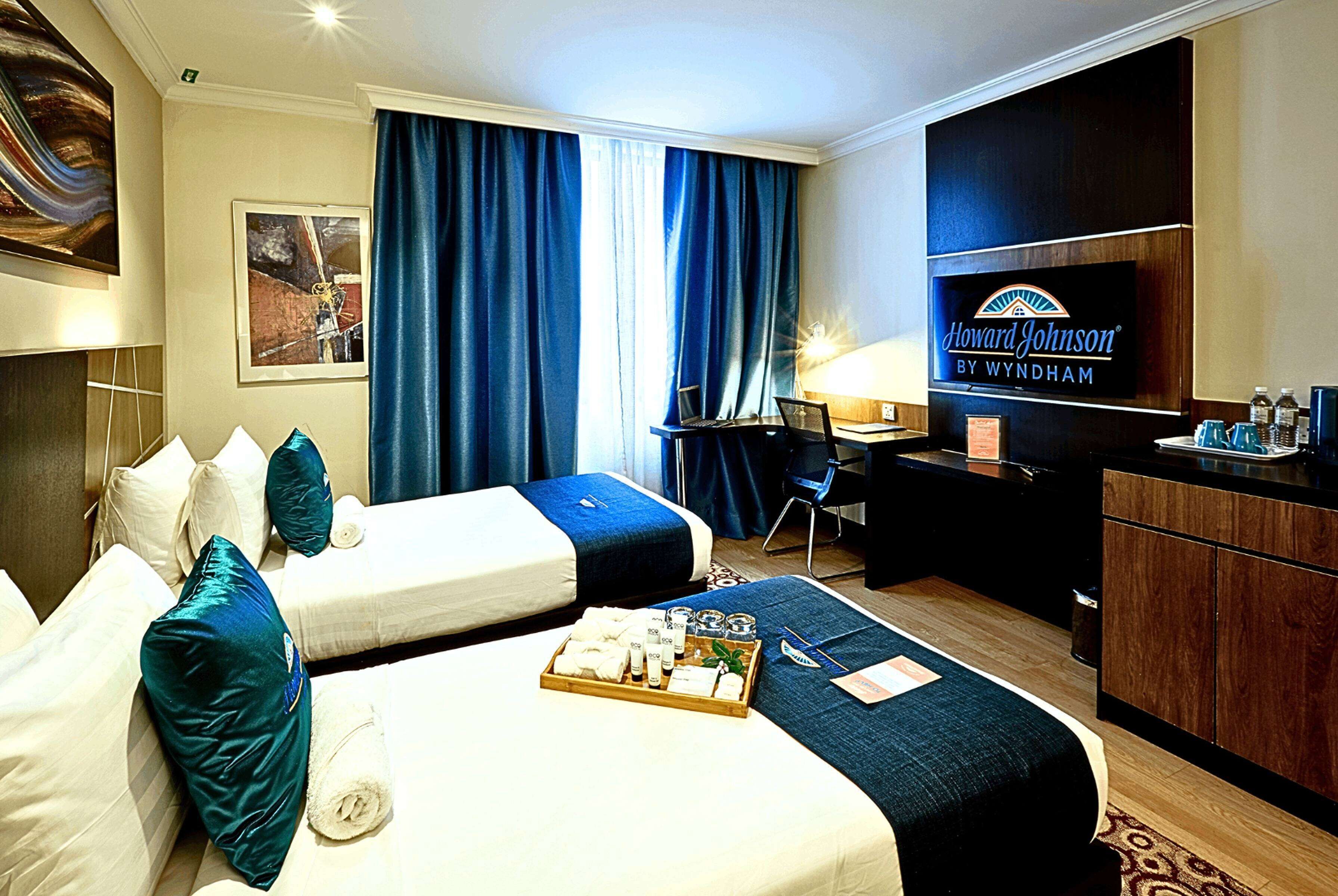 A hotel room with two beds, a desk, a TV, and a minibar.
