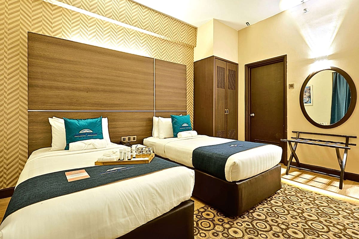 A hotel room with two beds, a wardrobe, a mirror, and a small table.