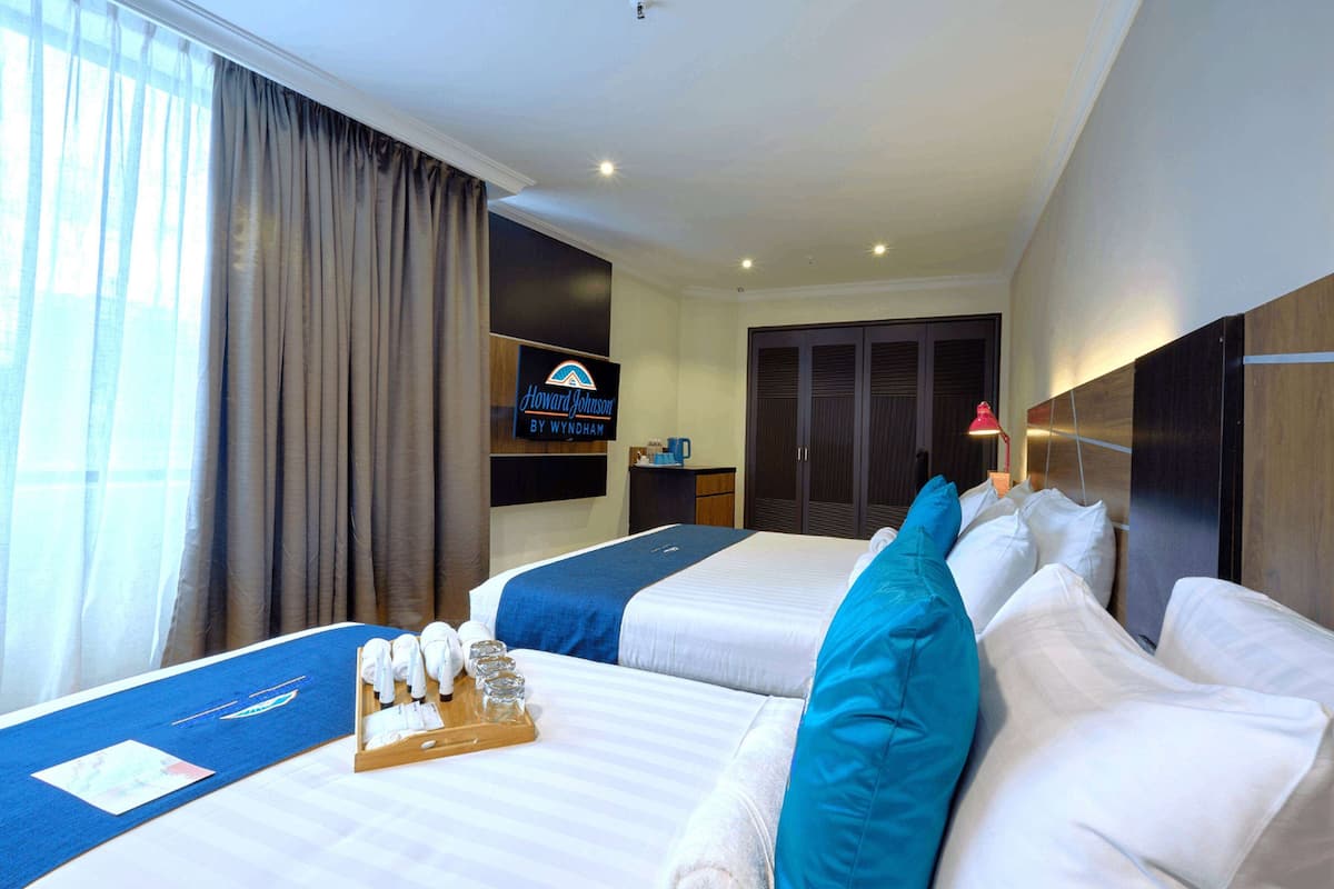 A hotel room with two beds, a desk, a wardrobe, and a sign for Howard Johnson by Wyndham.