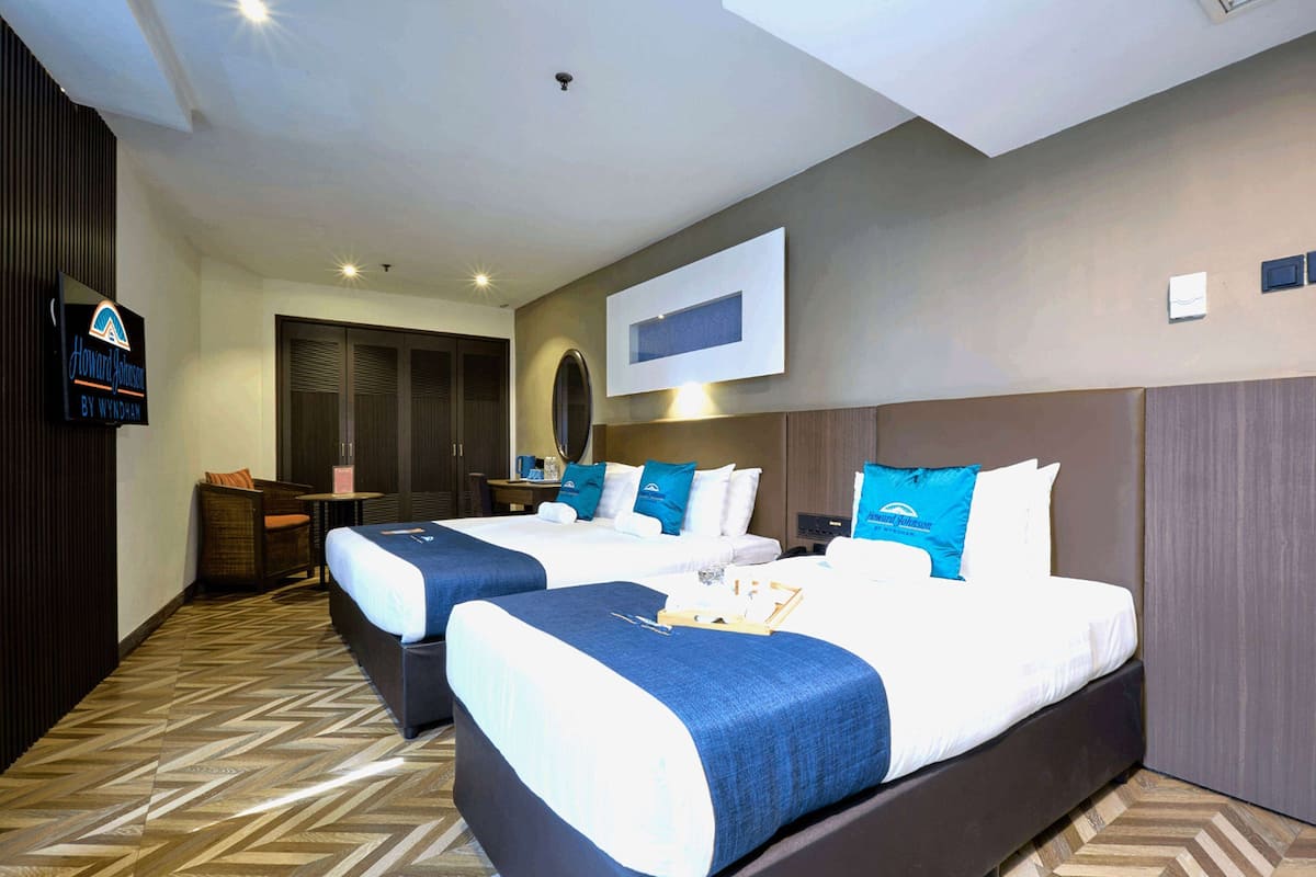 A hotel room with two beds, a desk, a chair, and a television.