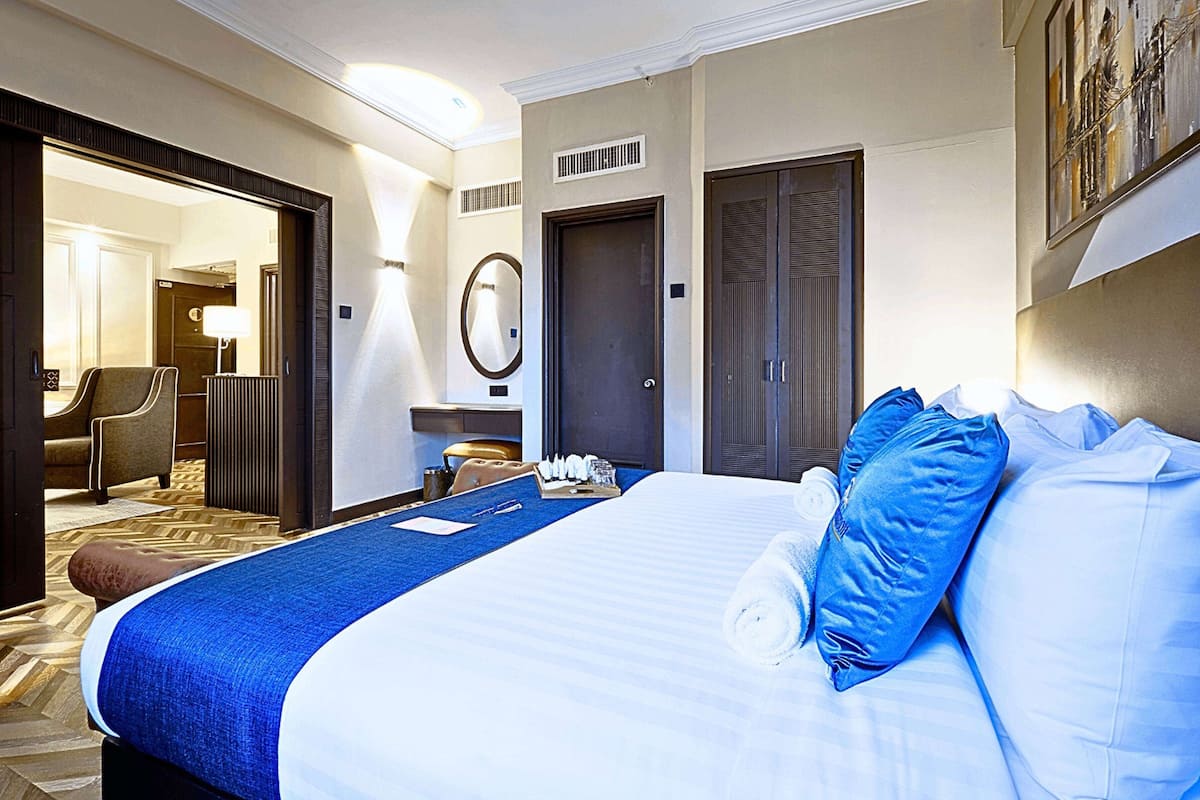 A hotel room with a large bed, a desk with a chair, a mirror, and a door.