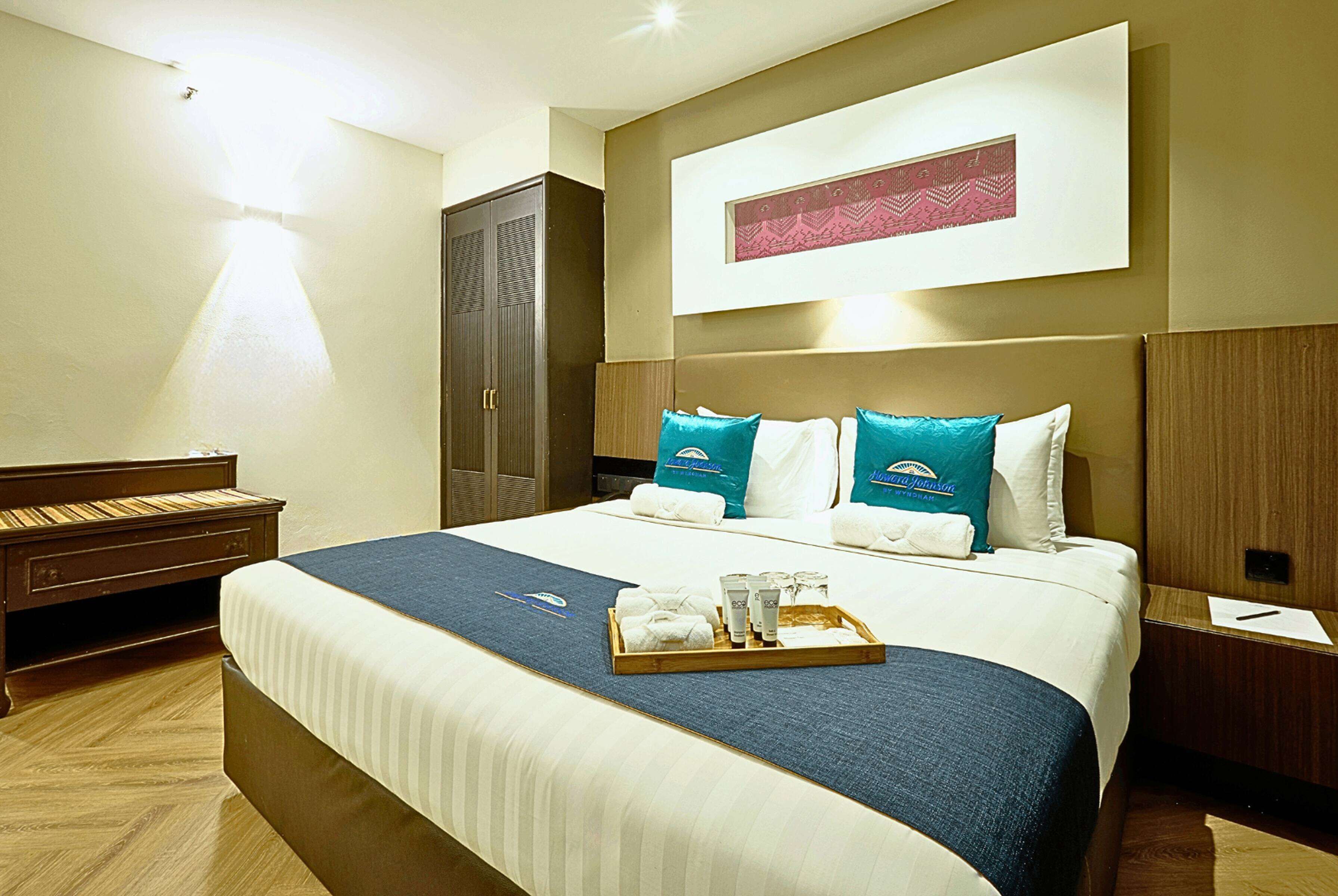 A hotel room with a large bed, a wooden nightstand, a wardrobe, and a wall-mounted artwork.