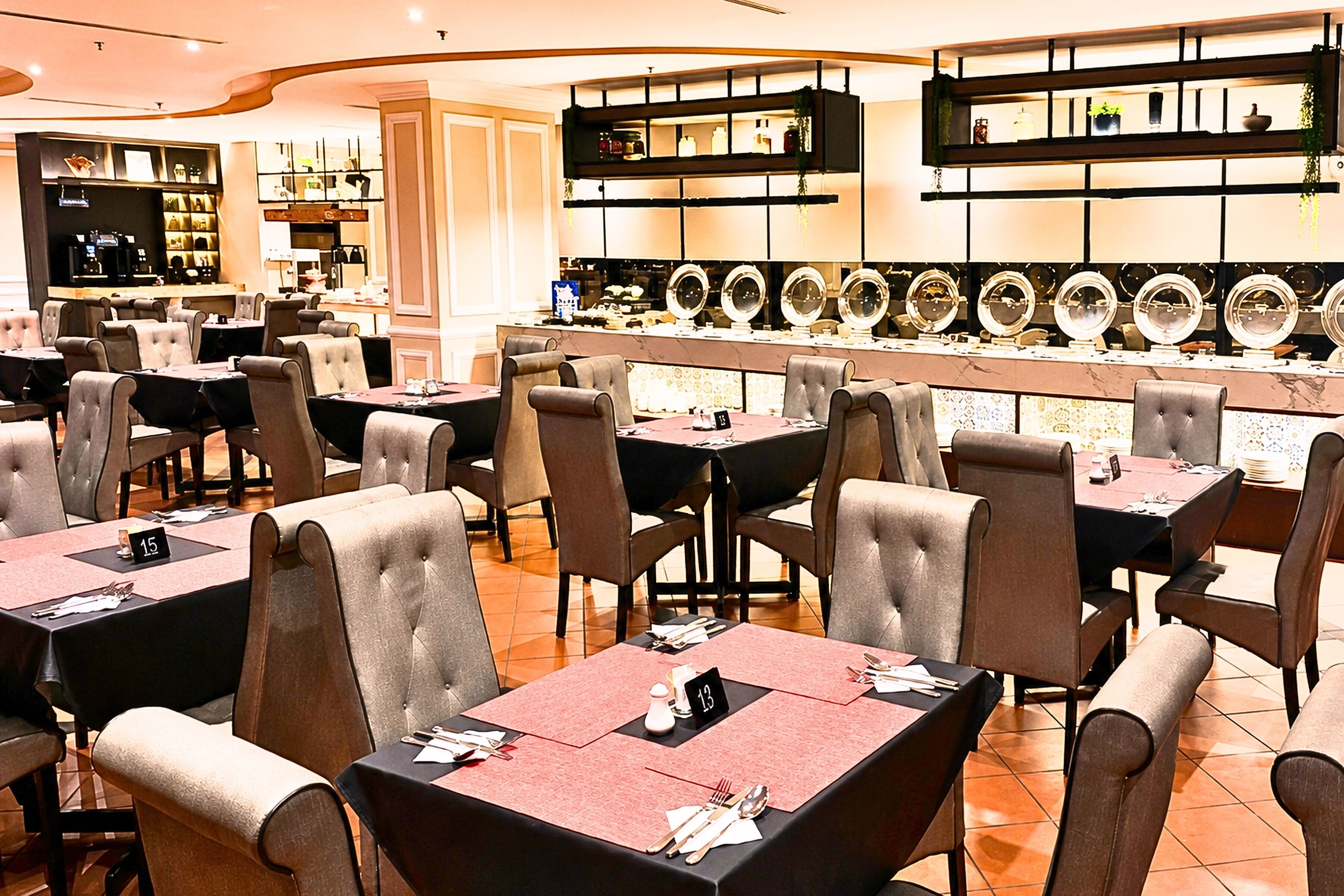 A restaurant with multiple tables and chairs, a bar area with mirrors, and a kitchen in the background.
